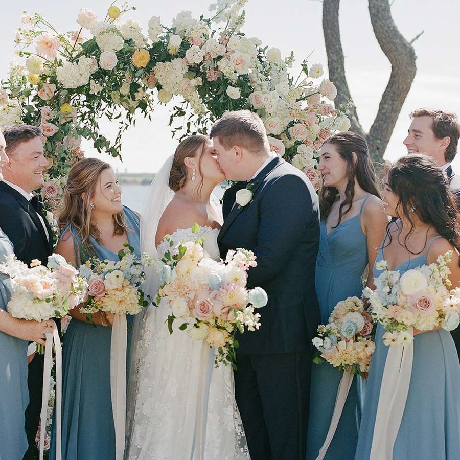 bride and groom kissing next to wedding party with tuxedos and blue dresses