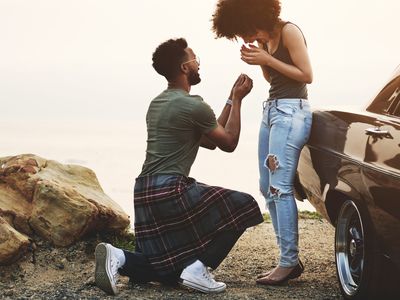 A man proposing to his girlfriend on a rocky terrain near their car