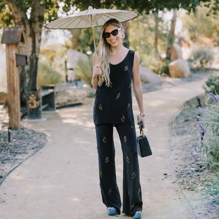 Wedding guest wearing a jumpsuit and holding a shade umbrella 