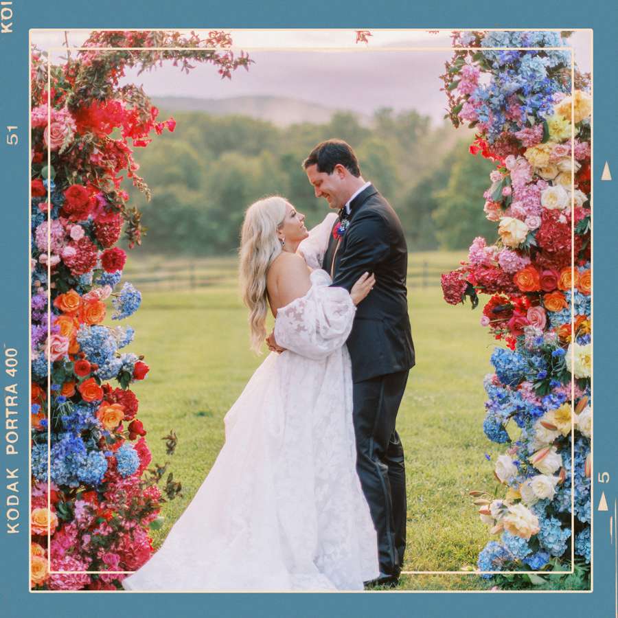 Bride and Groom Standing Next to Colorful Flower Arch