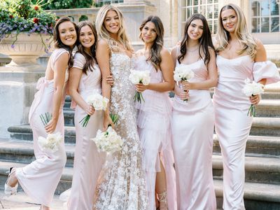 bride posing with her bridesmaids who are wearing light pink mismatched dresses