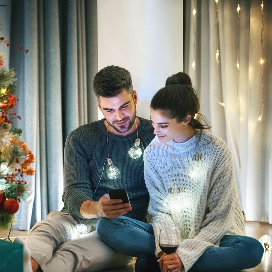 Closeup of couple sitting on the floor, having some wine and texting to friends and family during christmas