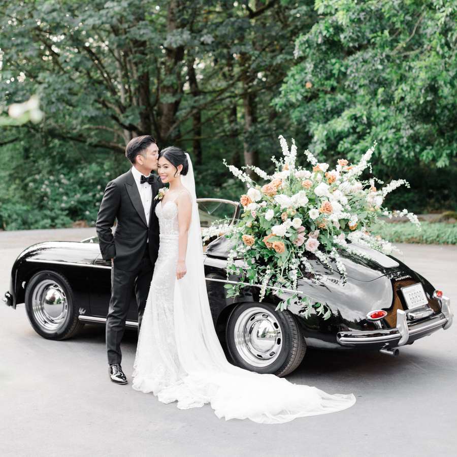 Groom Kissing Bride on the Temple While Standing Next to Vintage Porsche Covered in Flowers