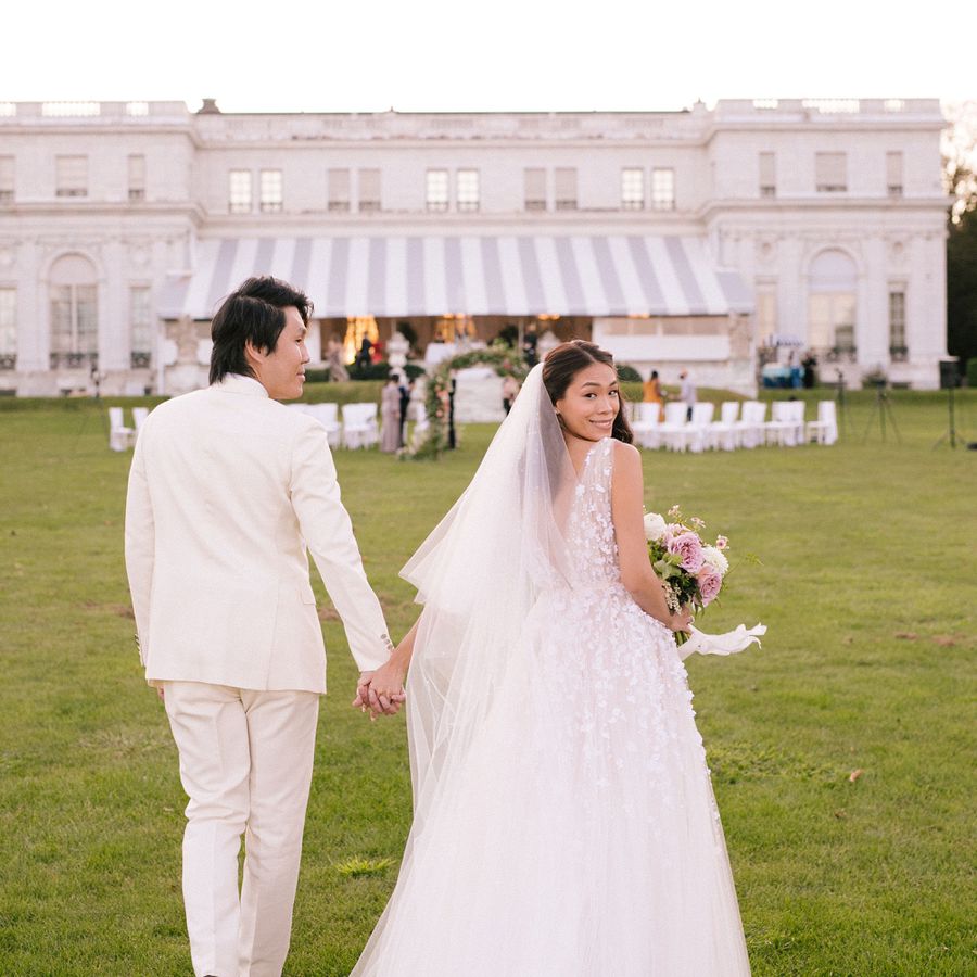 Bride in Floral Wedding Dress and Groom in White Suit Outside Rhode Island Mansion Wedding Venue