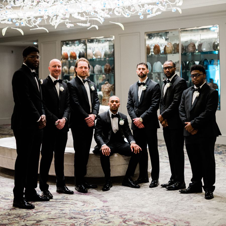 groom and groomsmen in black tuxedos posing for portrait in hotel
