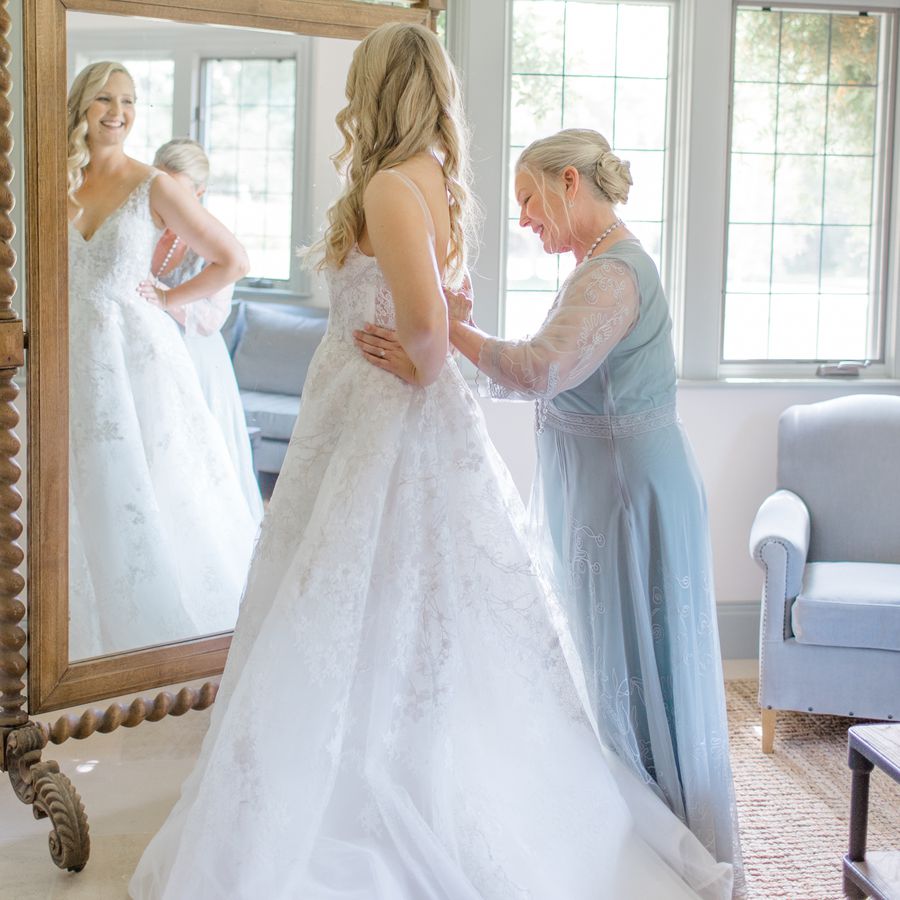 Mother-of-the-bride in blue gown fastens buttons on bride's dress