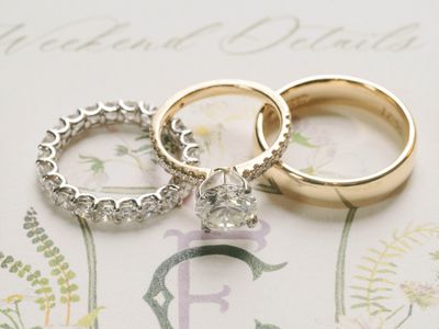 close up of a trio of rings: silver diamond eternity band; solitaire gold diamond engagement; gold wedding band