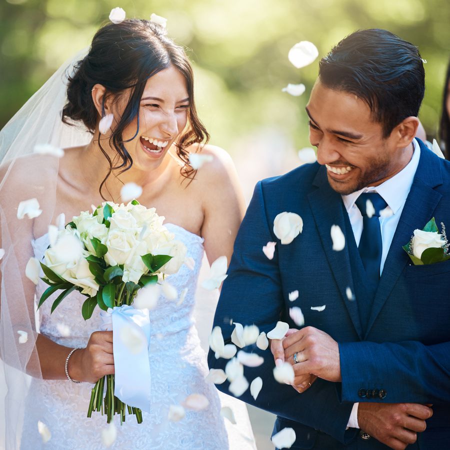 Bride and groom beaming and linking arms on their wedding day while guests toss flower petals