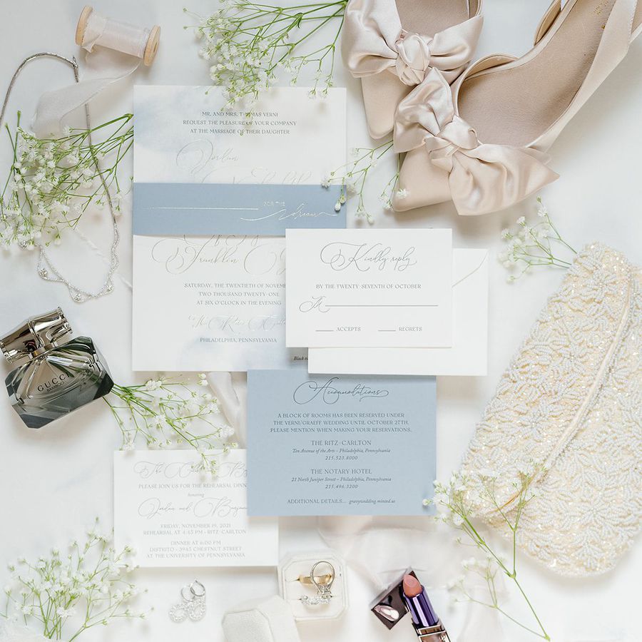 Blue, white, and silver wedding invitation flatlay, paired with beaded clutch and satin shoes