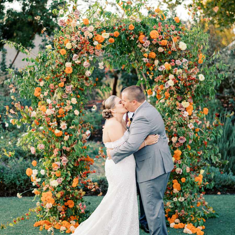 Bride and groom sharing their first kiss in front of a floral arch at their ceremony altar