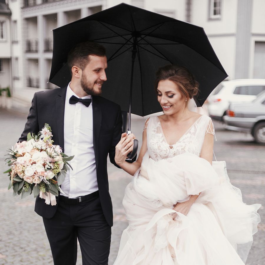 Bride and groom holding an umbrella during their rainy wedding day