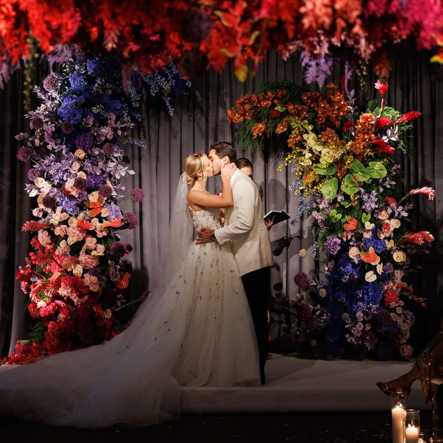 Bride and Groom Kissing in Front of Rainbow-Colored Floral Ceremony Arch