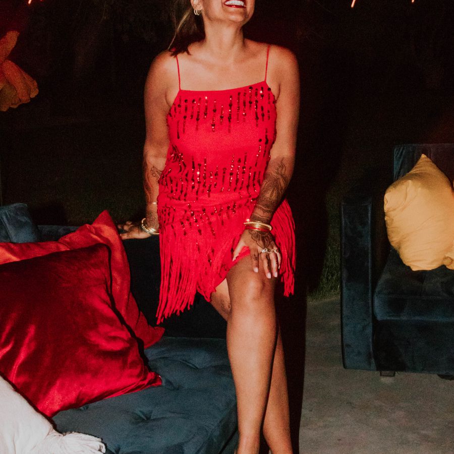 woman wearing a red sequin and fringe mini dress while sitting on a couch