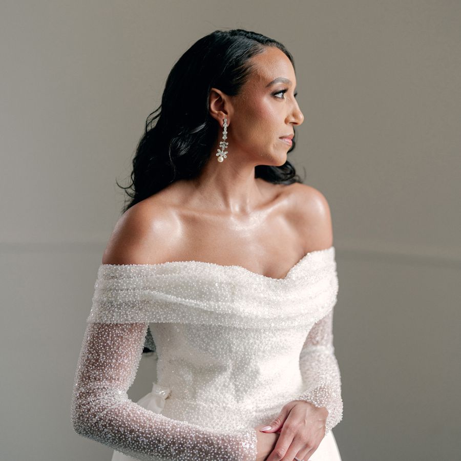 bride with romantic loose waves, crystal earrings, and off-the-shoulder beaded wedding dress
