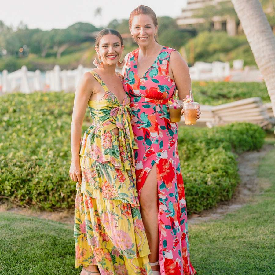Two people posing in colorful floral dresses and holding drinks