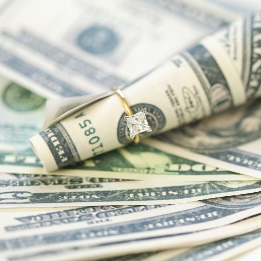 a solitaire wedding ring wrapped around a $100 bill
