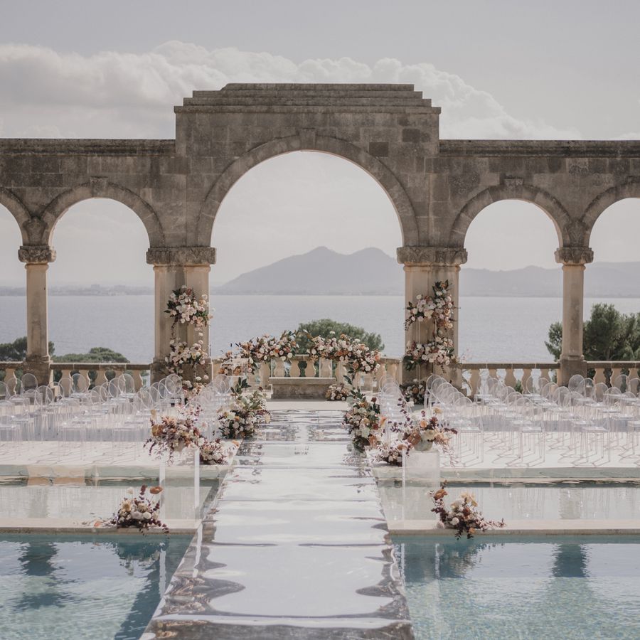 Outdoor wedding venue with fresh pink flower arrangements, in-ground pools, and stone arches overlooking the ocean.